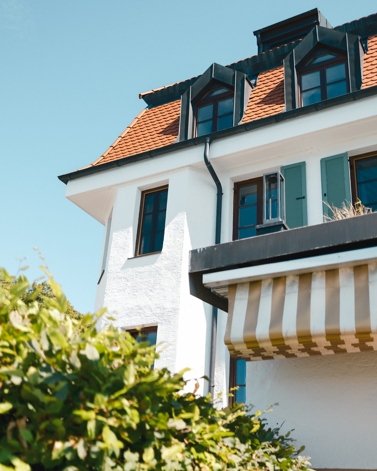 Das weiße Hotelgebäude mit roten Dachziegeln, Gauben und grünen Fensterläden