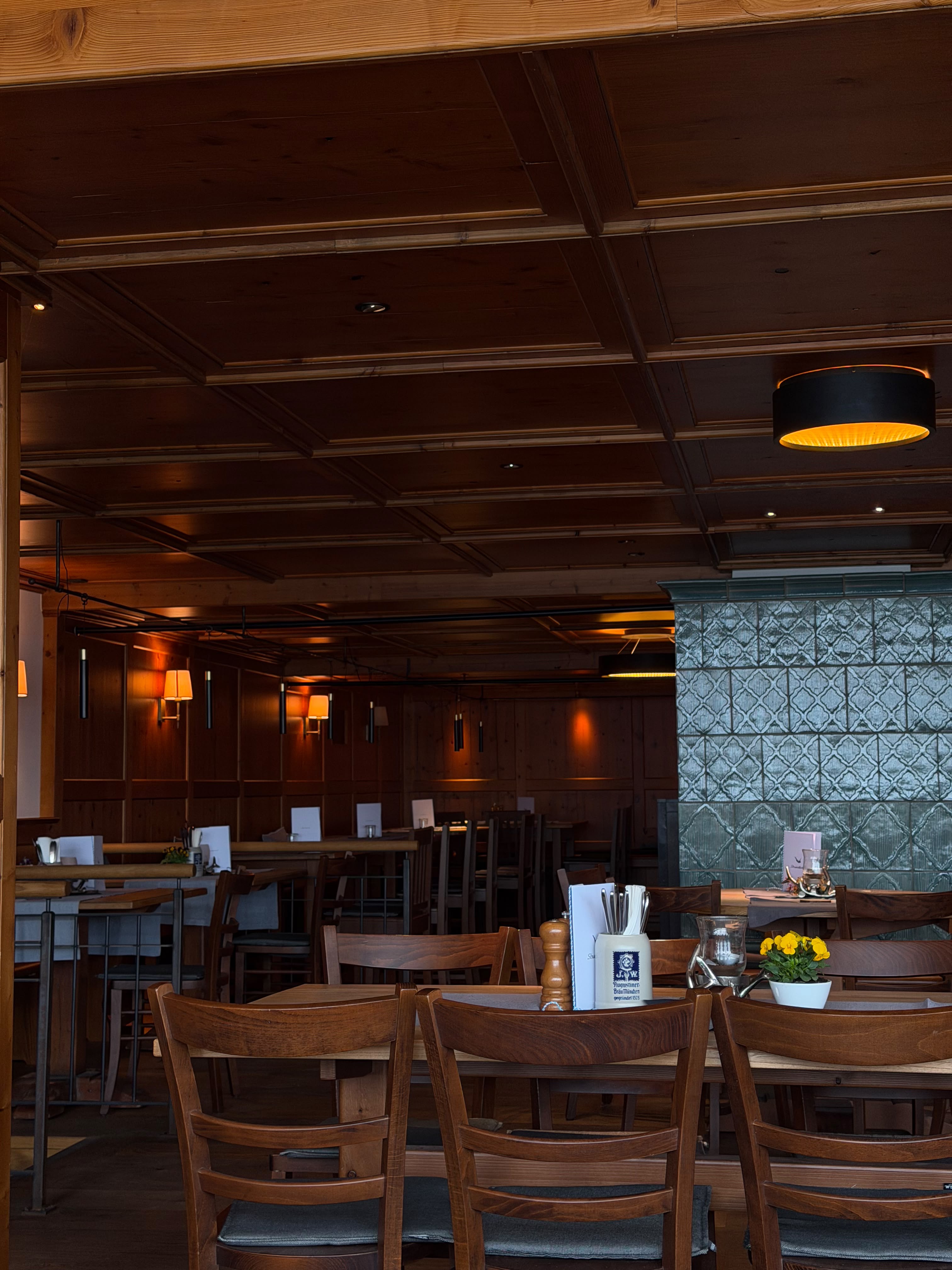 Gemütliche Stube im Strandhotel mit Holztischen, dunklen Holzstühlen, warmer Beleuchtung und dekorativem Ofen.